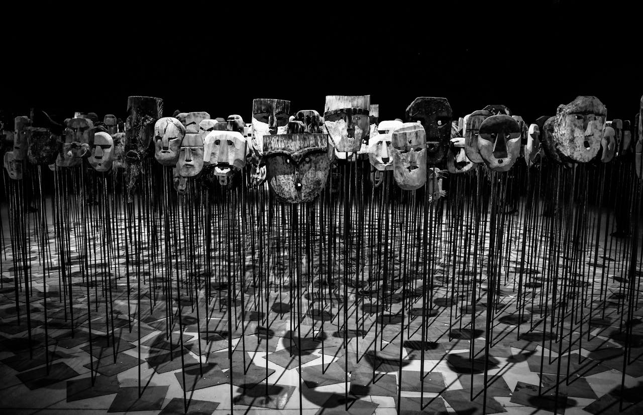 An artistic display of wooden masks on poles, set in a dimly lit theater.